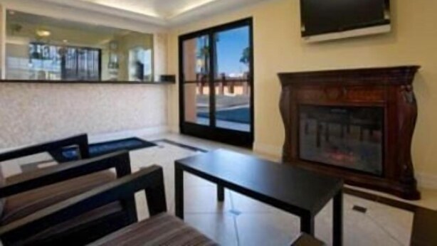 Quarto de hotel com uma janela ampla, televisão de tela plana na parede, lareira de madeira e um espaço de estar com um banco e uma mesa.