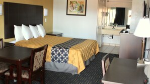 Quarto de hotel com cama, escrivaninha, cadeira, abajur, espelho e pintura na parede.