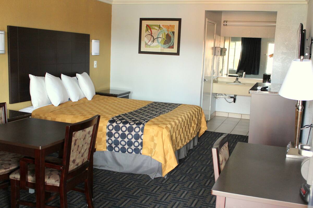 Een hotelkamer met een bed, een bureau, een stoel, een lamp, een spiegel en een schilderij aan de muur.