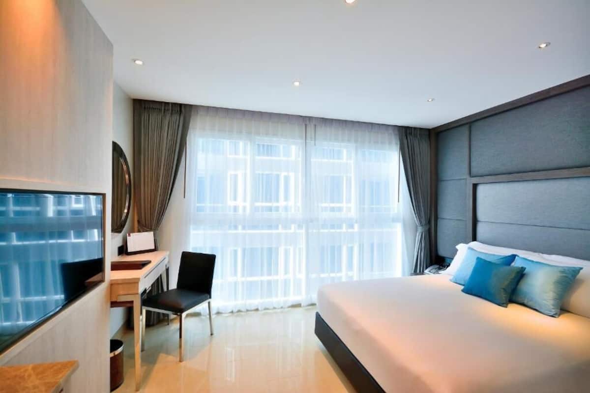 A modern hotel room with a large bed, a desk, and a TV.