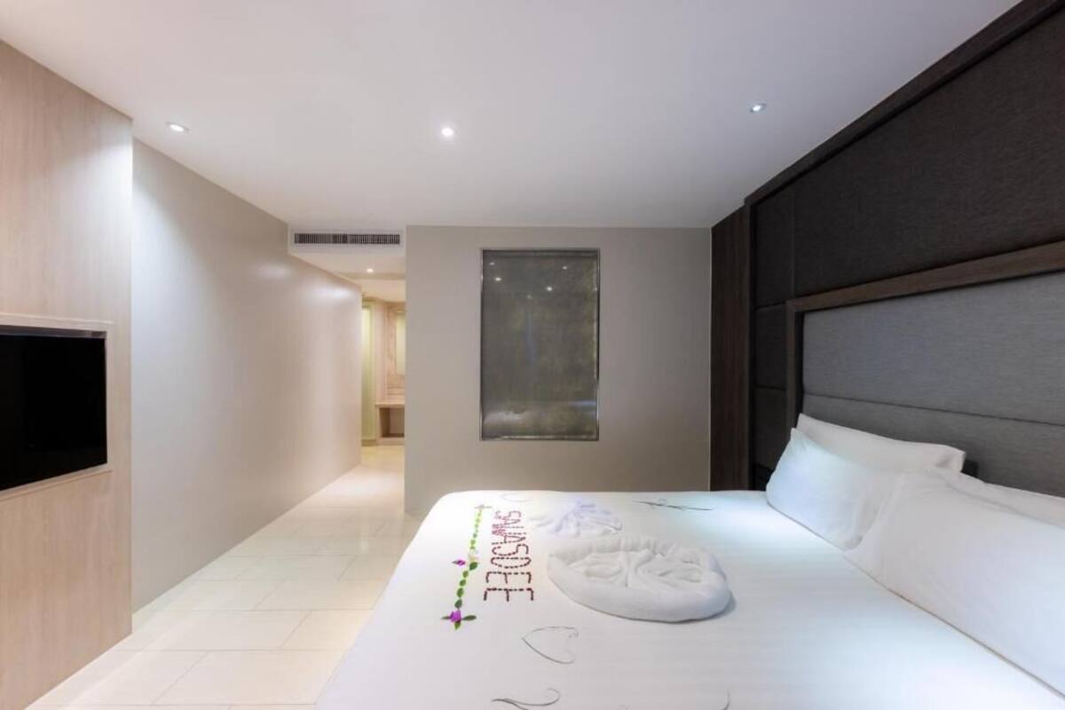 A modern hotel room with a large bed, a flat-screen TV mounted on the wall, and a small window.