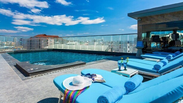 Un área de piscina en la azotea con sillones reclinables azules, una piscina pequeña y una barandilla de cristal.