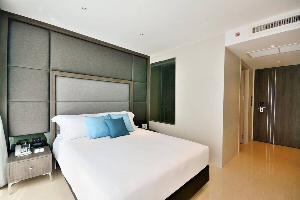 A modern hotel room with a large bed, a nightstand, a wall-mounted TV, and a door leading to another room.