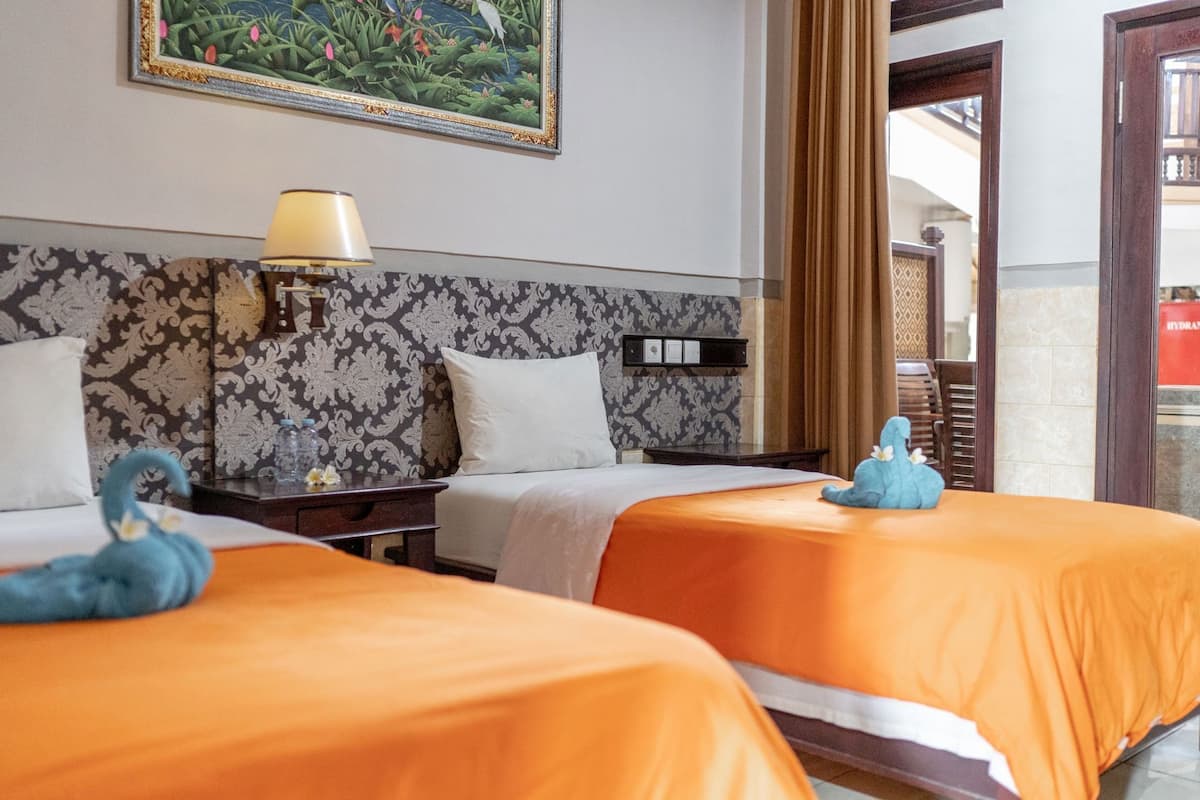 A hotel room with two beds, a nightstand, a lamp, a framed painting, and a view of the outside.