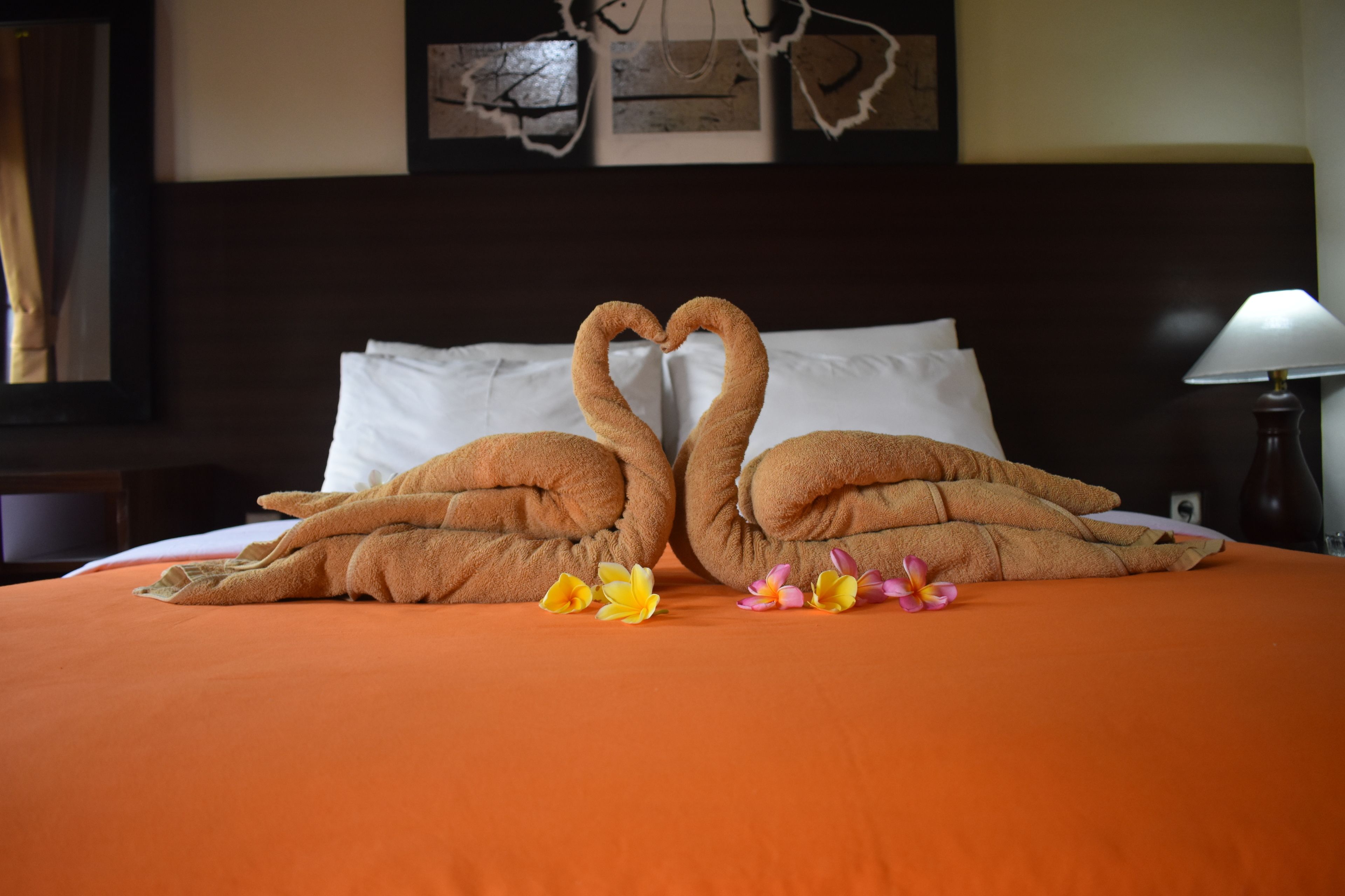 Una cama con dos toallas dobladas en forma de cisnes y algunas flores sobre un edredón naranja.