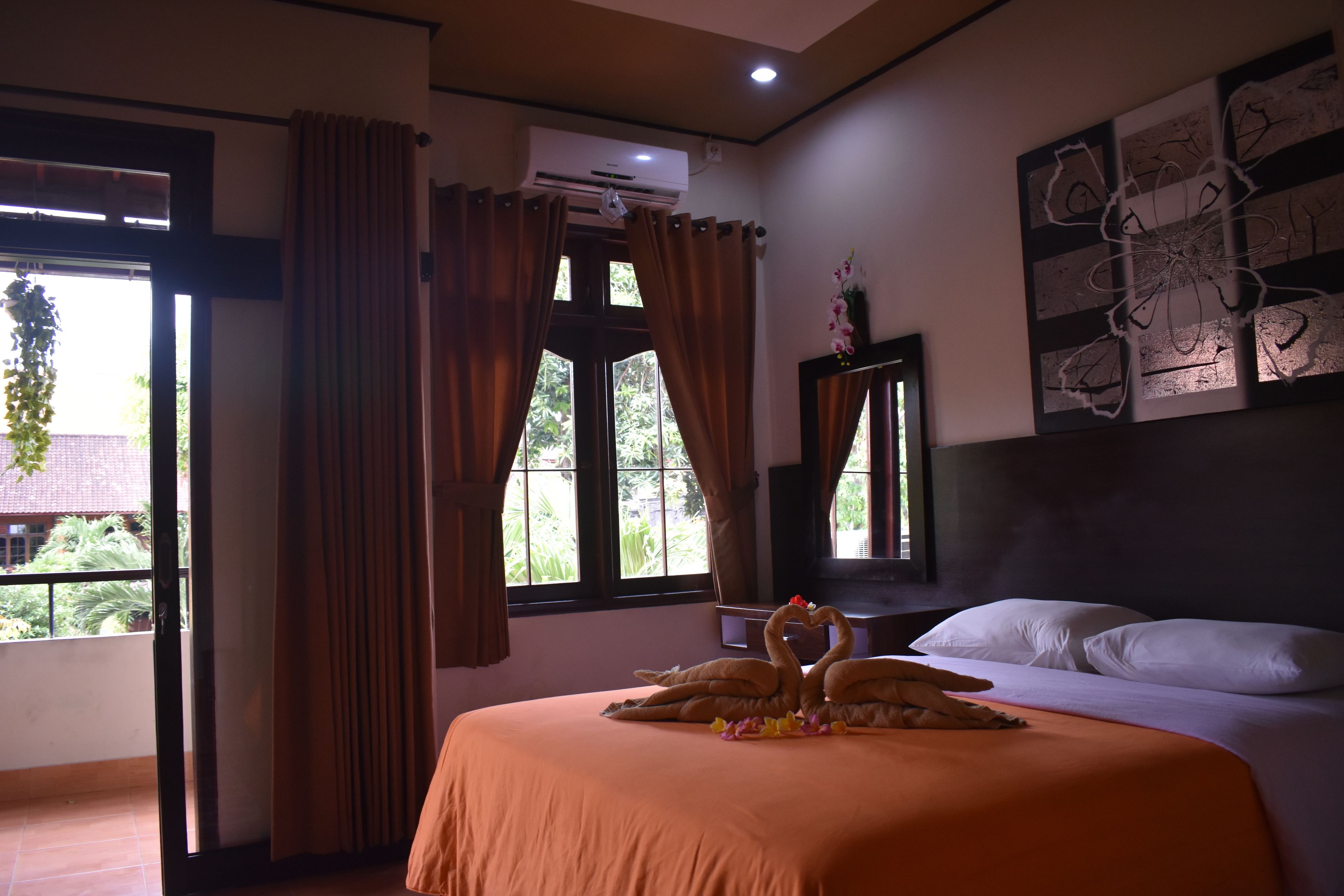 A hotel room with a bed, a window with curtains, an air conditioning unit, and a wall with artwork.