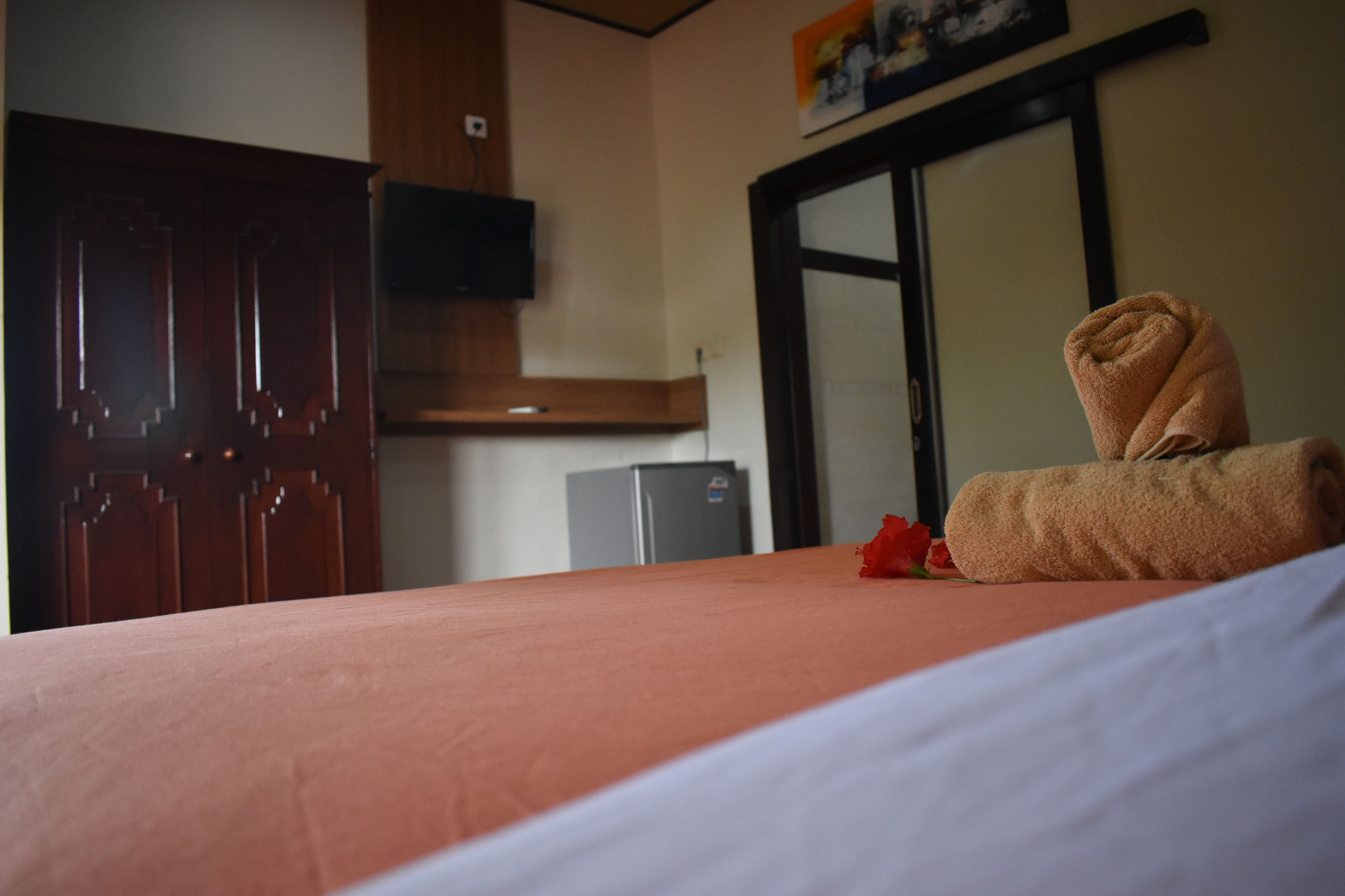 Een hotelkamer met een bed, een houten garderobe, een aan de muur bevestigde televisie en een deur met een ruit.