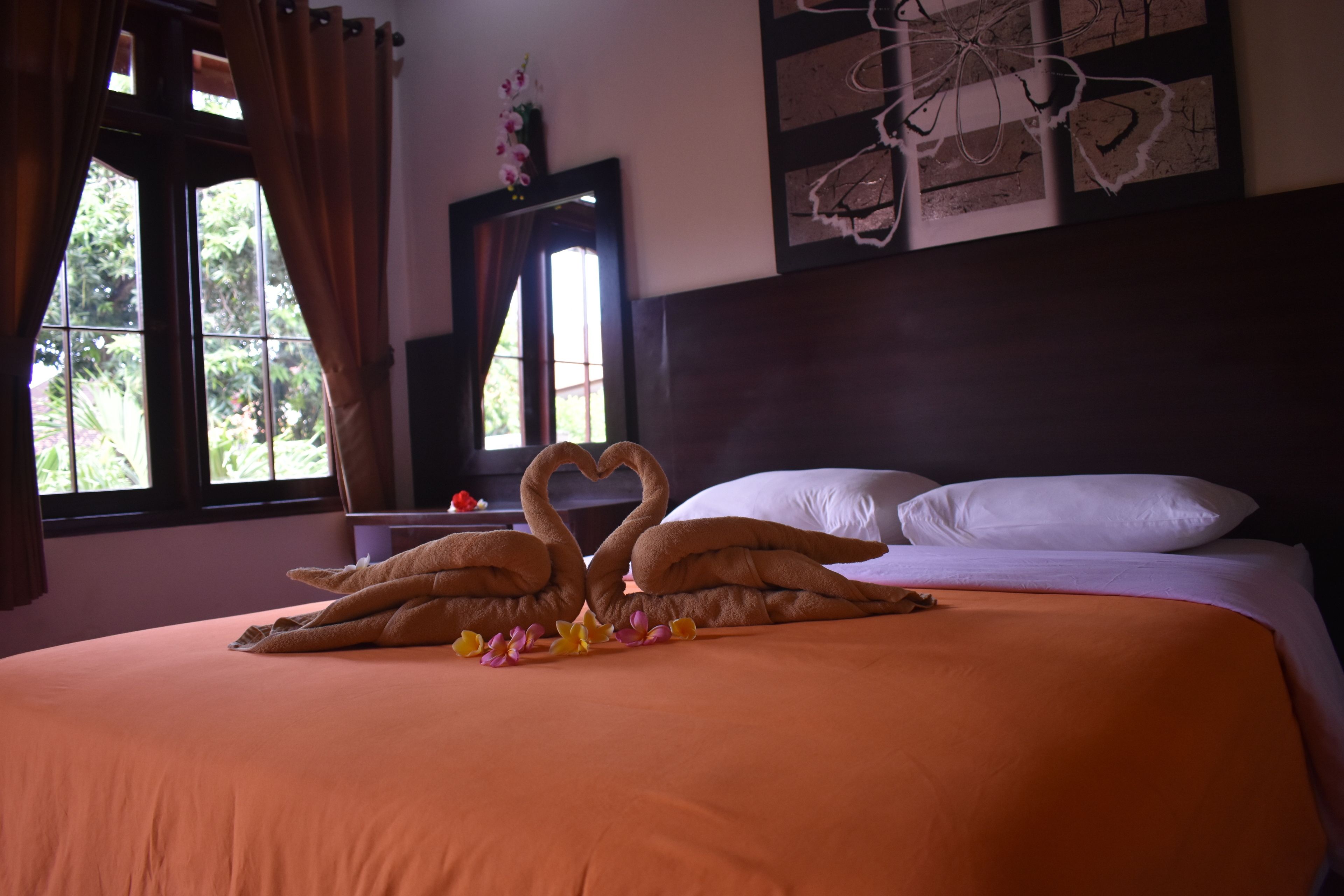 A neatly made bed with a heart-shaped towel arrangement and a bouquet of flowers.