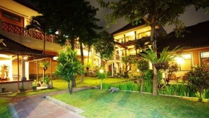 A hotel with a well-maintained lawn, outdoor seating area, and multiple balconies. - Bendesa Accommodation (Kuta)
