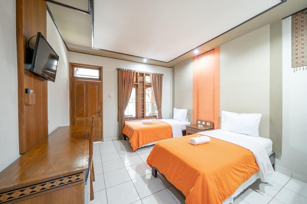 A hotel room with two beds, a wooden desk, a television, and a window with curtains.
