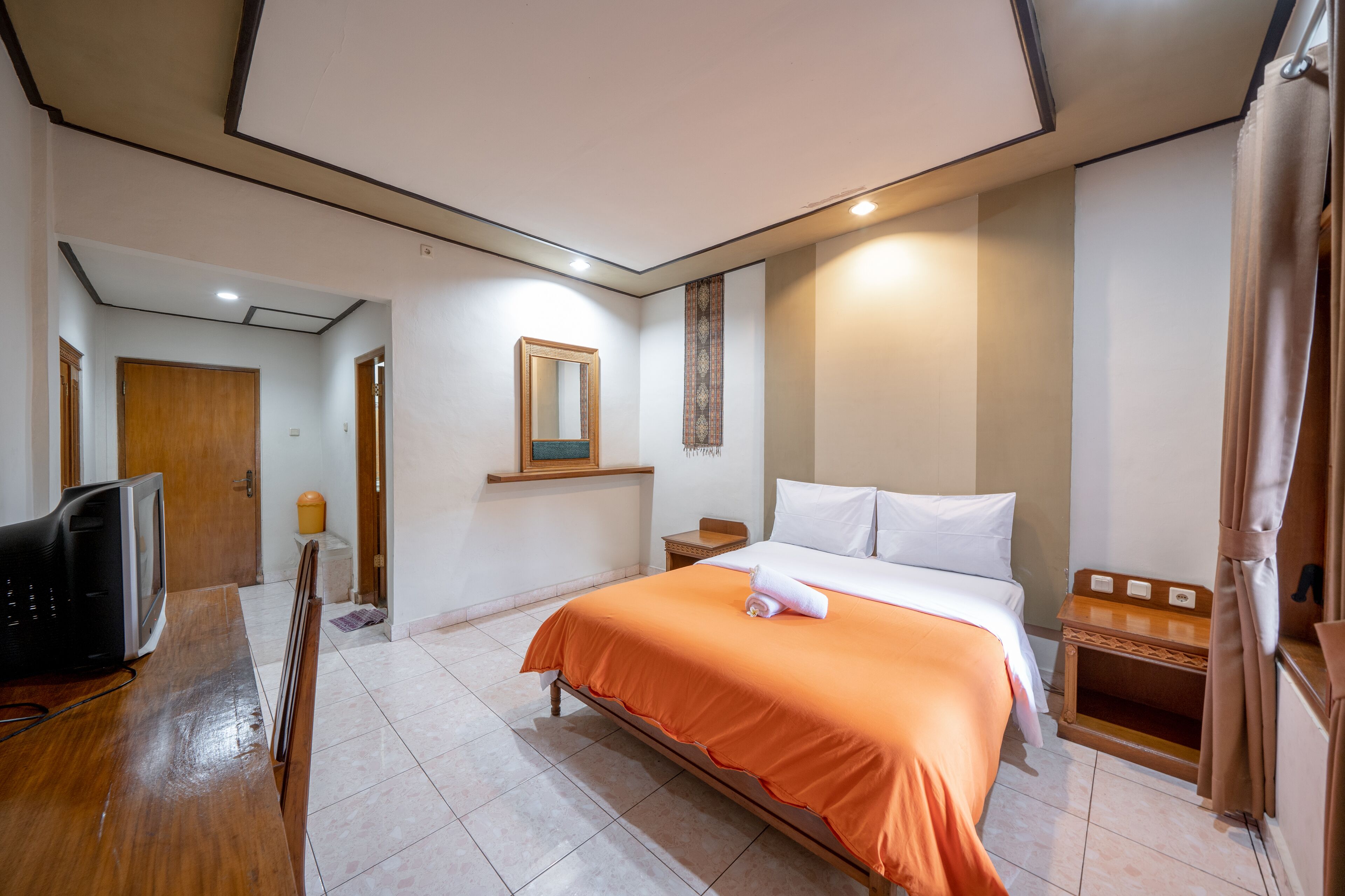 A hotel room with a bed, a television, a wooden desk, and a mirror.