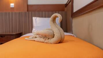 Uma cama com um cobre-leito laranja e uma toalha em forma de cisne.