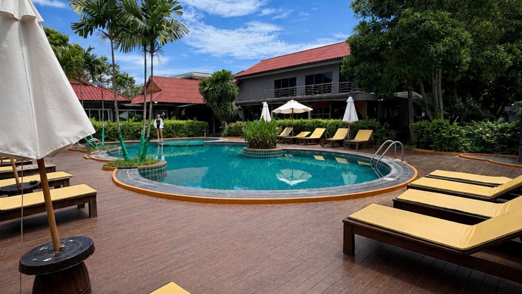 A pool area with lounge chairs, a pool, and a building in the background.