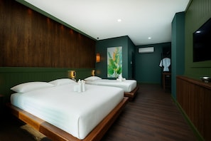 A hotel room with two beds, a wooden headboard, a green accent wall, a painting, and a TV on the wall. - Tuana Hotels The Natural Resort (Patong)