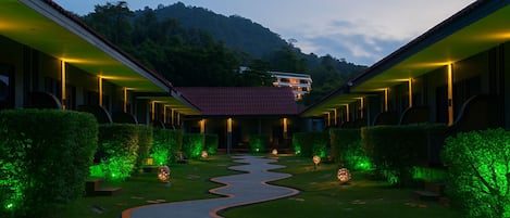 Un hotel con un patio central, rodeado de edificios con barandillas iluminadas, y una montaña al fondo.