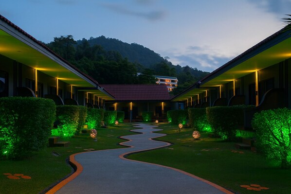 Un hotel con un patio central, rodeado de edificios con barandillas iluminadas, y una montaña al fondo.
