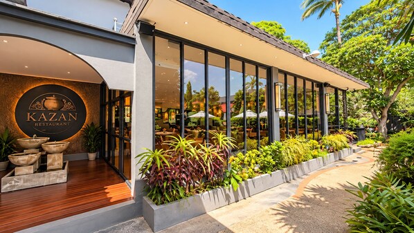 Un restaurante con fachada moderna, amplios ventanales y terraza al aire libre con plantas.
