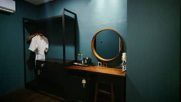Una habitación compacta con cama, un escritorio pequeño, un espejo y un armario.