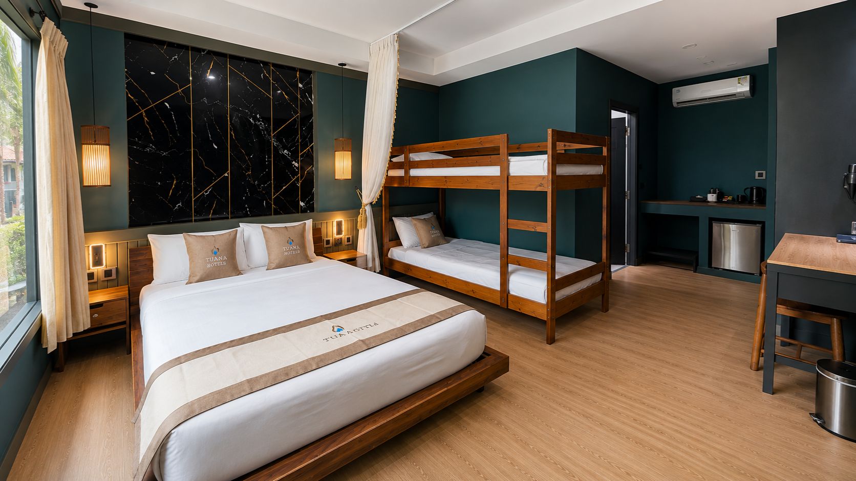 A hotel room with a large bed, a bunk bed, a desk, and a kitchenette.