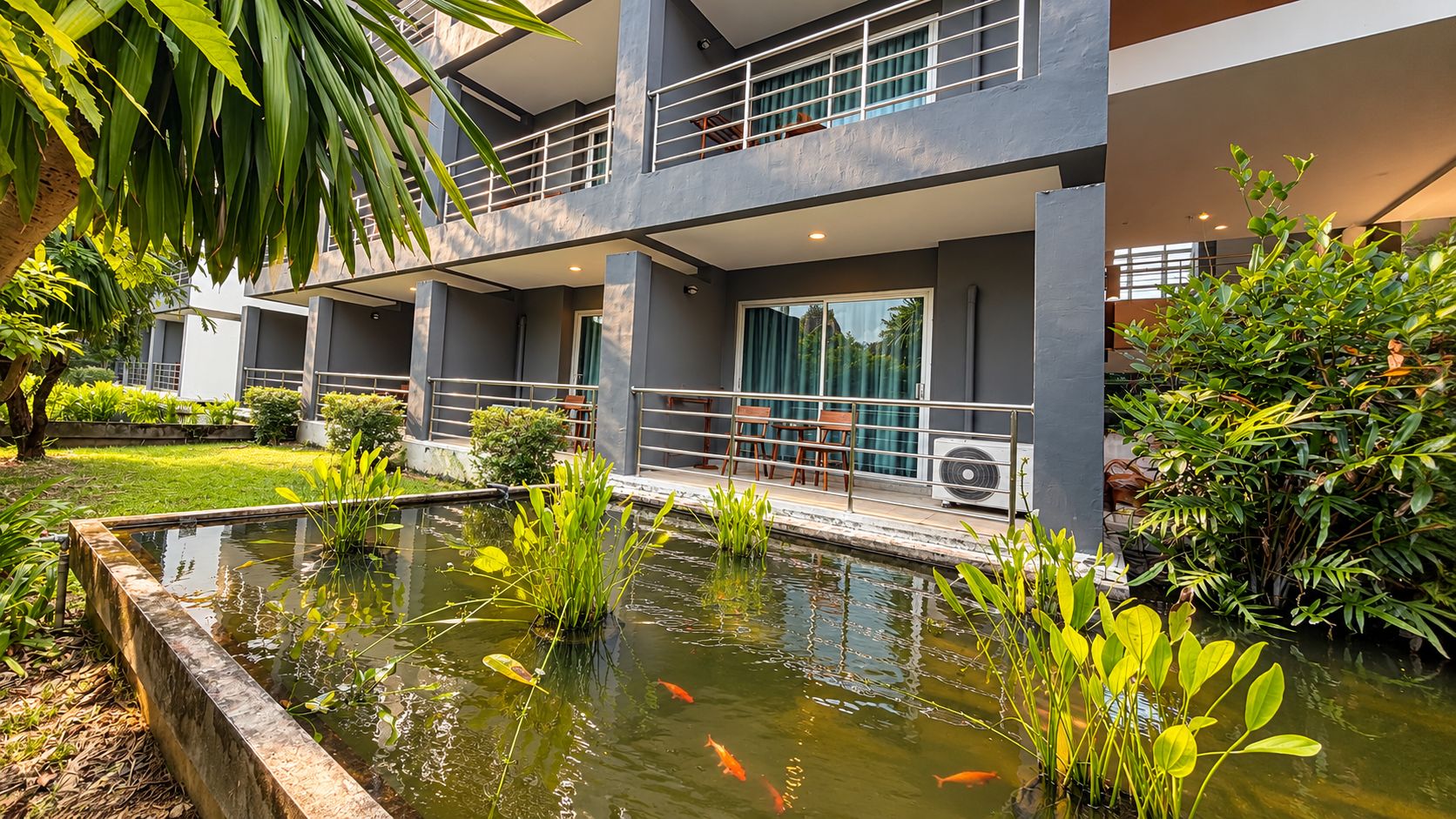 A modern building with a rooftop terrace, a small pond with koi fish, and surrounding greenery.