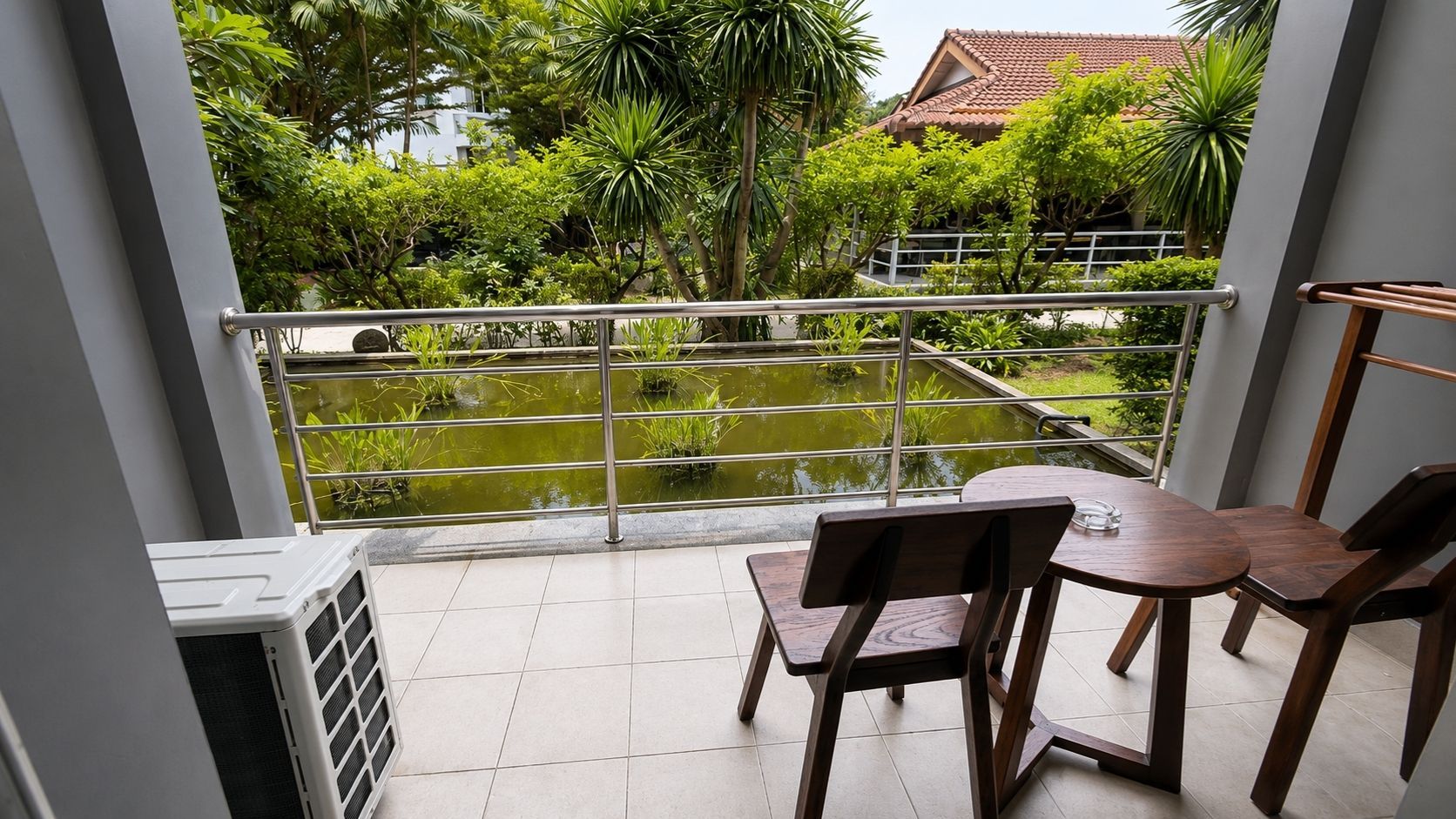 A balcony with a view of a garden and a pond, featuring a table and chairs.