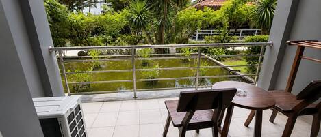 A balcony with a view of a garden and a pond, featuring a table and chairs.