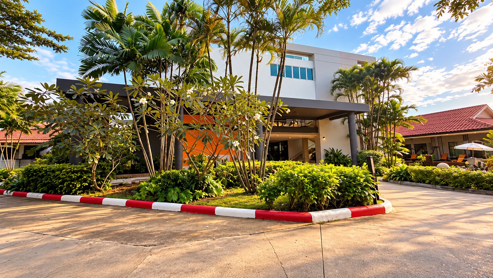 A modern building with a covered entrance, surrounded by well-maintained greenery and a red and white curbed driveway.