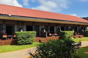 A hotel with a red-tiled roof, outdoor seating with wooden tables and chairs, and well-maintained greenery. - Tuana Hotels The Natural Resort (Patong)