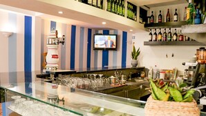 A bar area with a television screen, shelves of bottles, and a glass display case with wine glasses. - Hotel Amparo (Machico)