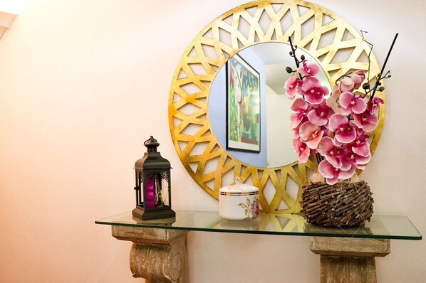A glass-top table with a decorative mirror, a lantern, and a vase with pink flowers. - Hotel Amparo (Machico)