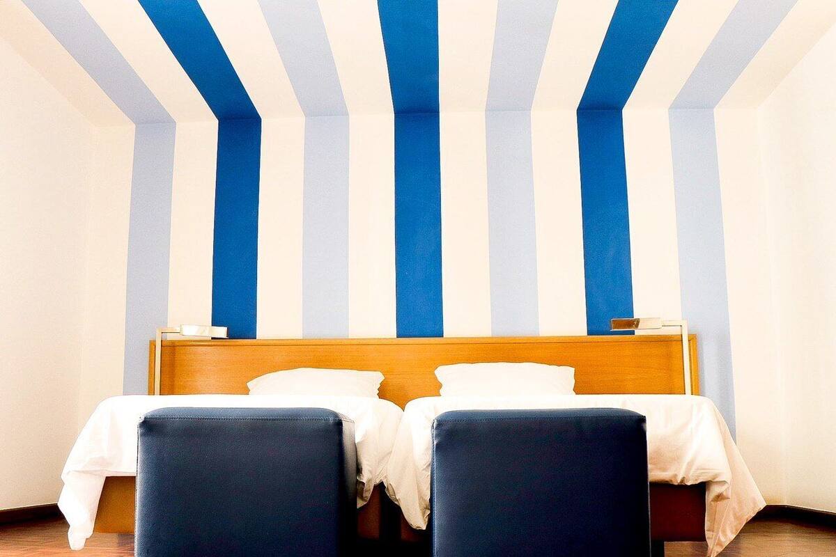A hotel room with a bed, two bedside tables, and a striped ceiling.