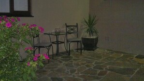 A stone-floored patio with a table and two chairs, a potted plant, and a window with blinds. - Sunnyridge Lodge (East London)