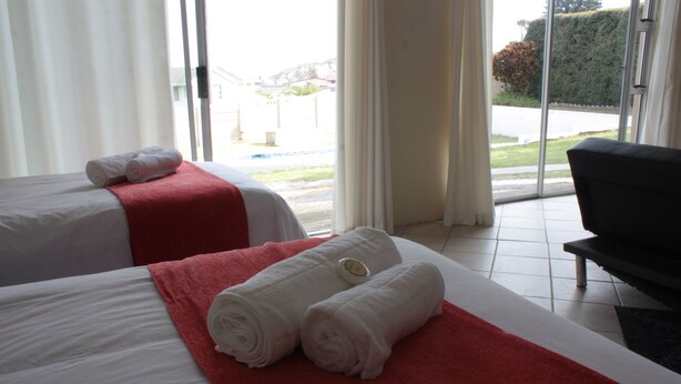 A hotel room with two beds, each with a red and white bedspread, and a black chair. - Sunnyridge Lodge (East London)