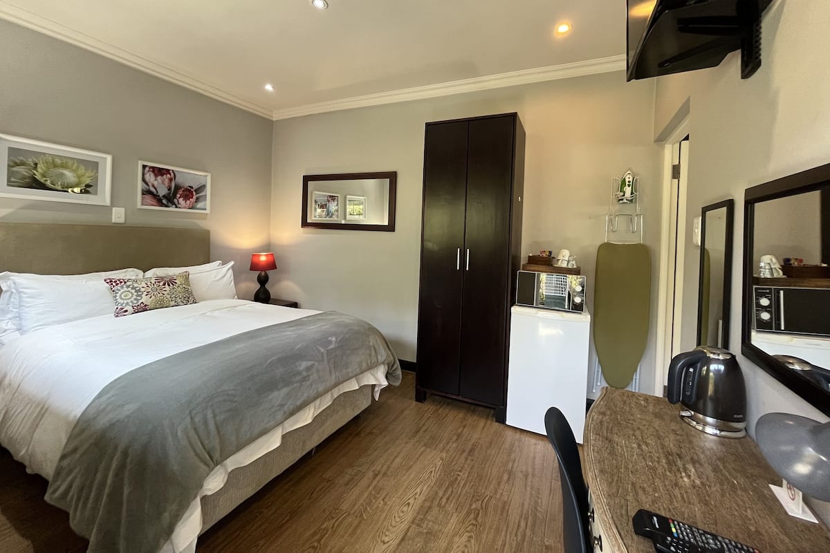 Quarto de hotel com cama, escrivaninha com chaleira, micro-ondas, espelho e guarda-roupa.