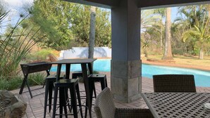 An outdoor patio with a pool, surrounded by greenery and palm trees. - Ilanda Guest House (Mbombela)