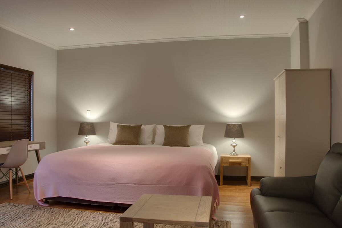 Quarto com cama, abajures, escrivaninha, cadeira, sofá e guarda-roupa.