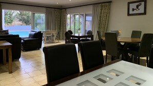 A spacious living area with a pool view, a dining table, and comfortable seating. - Ilanda Guest House (Mbombela)