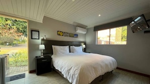 A bedroom with a bed, nightstands, a window, and a door leading to a garden. - Ilanda Guest House (Mbombela)