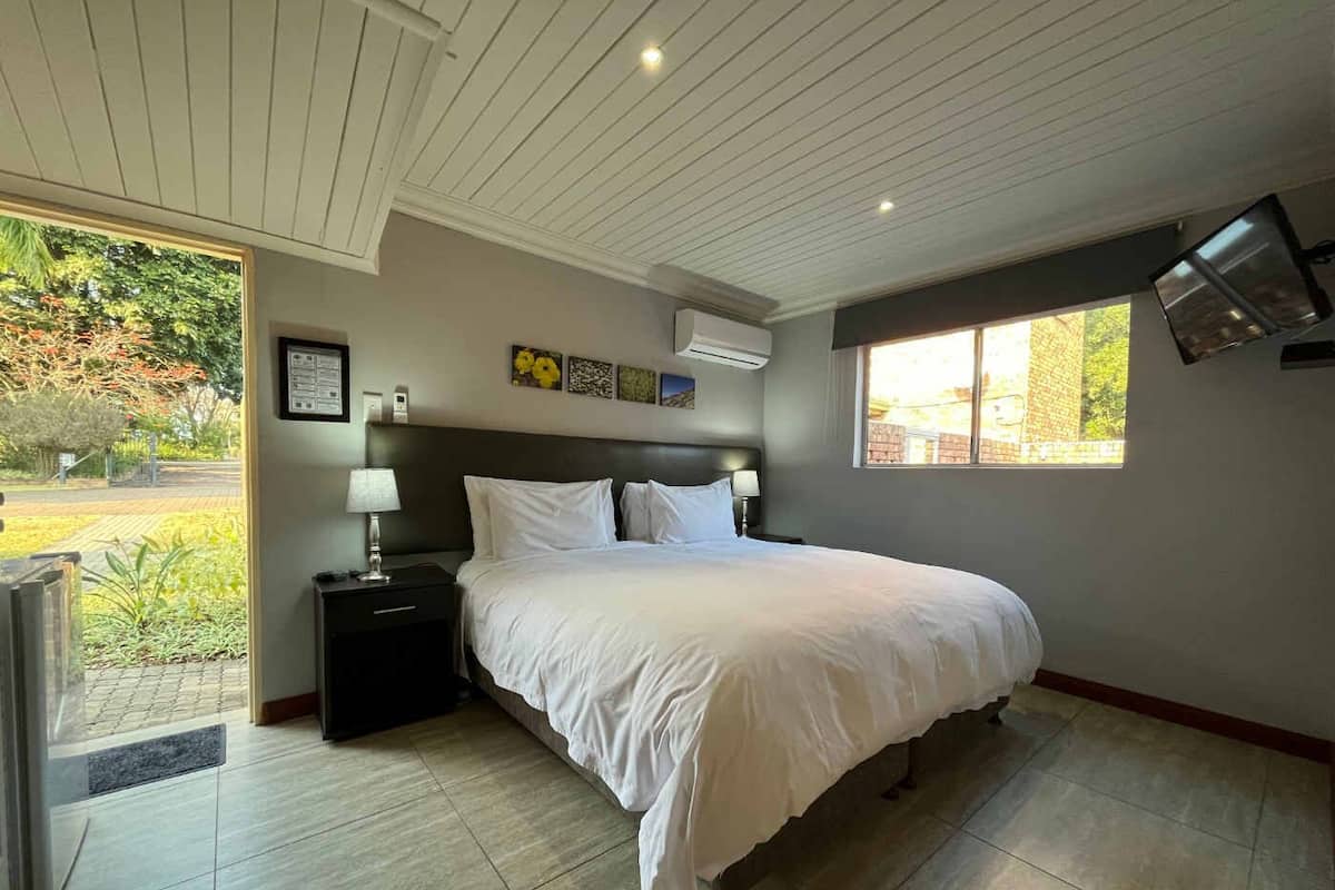 Quarto com cama, mesas de cabeceira, uma janela e uma porta que dá para um jardim.
