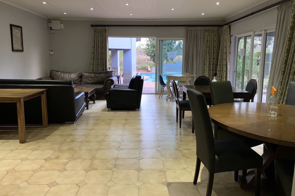 Quarto espaçoso com sofá, cadeiras, mesa de jantar e vista para uma piscina através de grandes janelas.