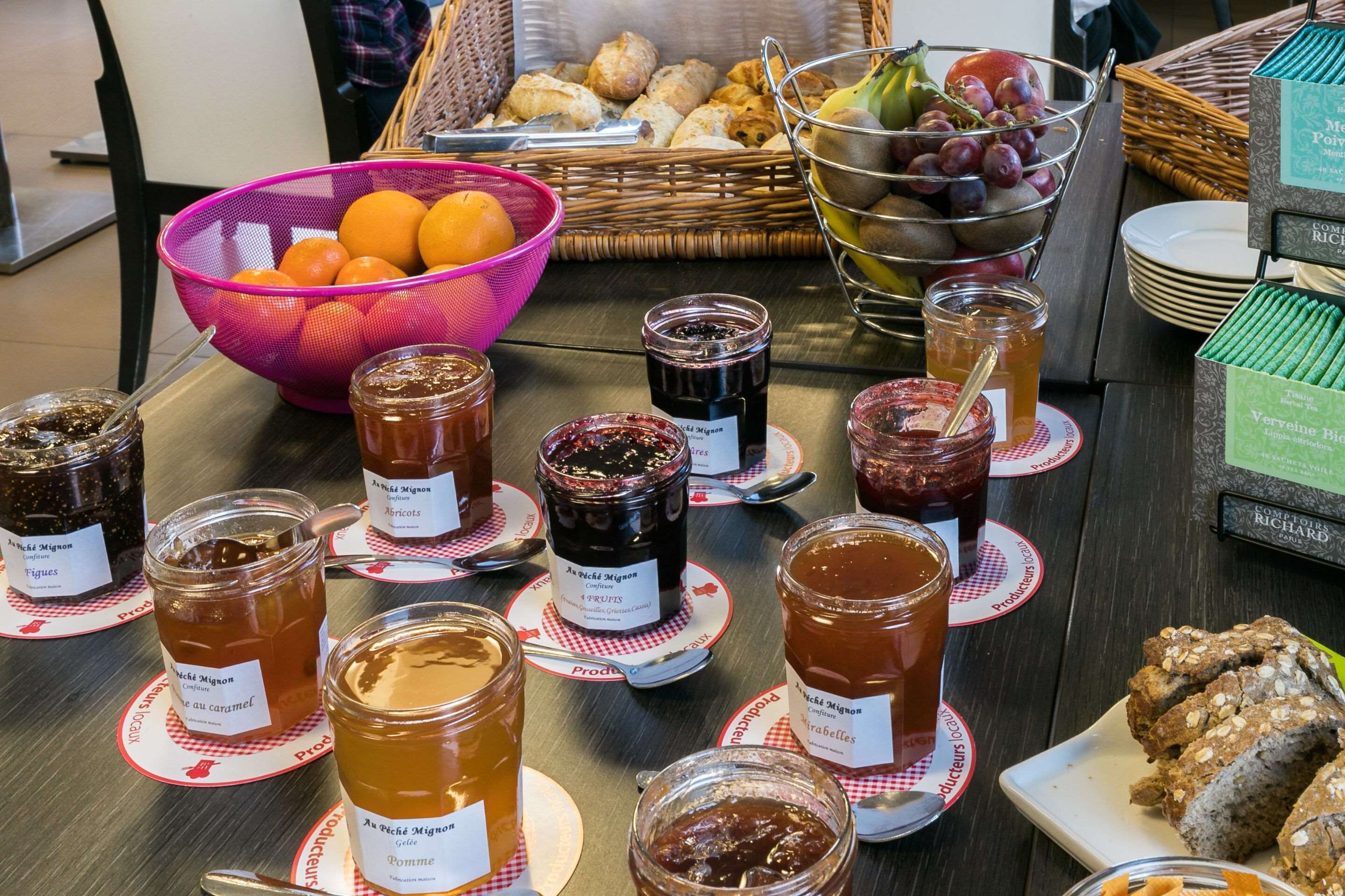 A table with various jars of preserves and a basket of fruits.