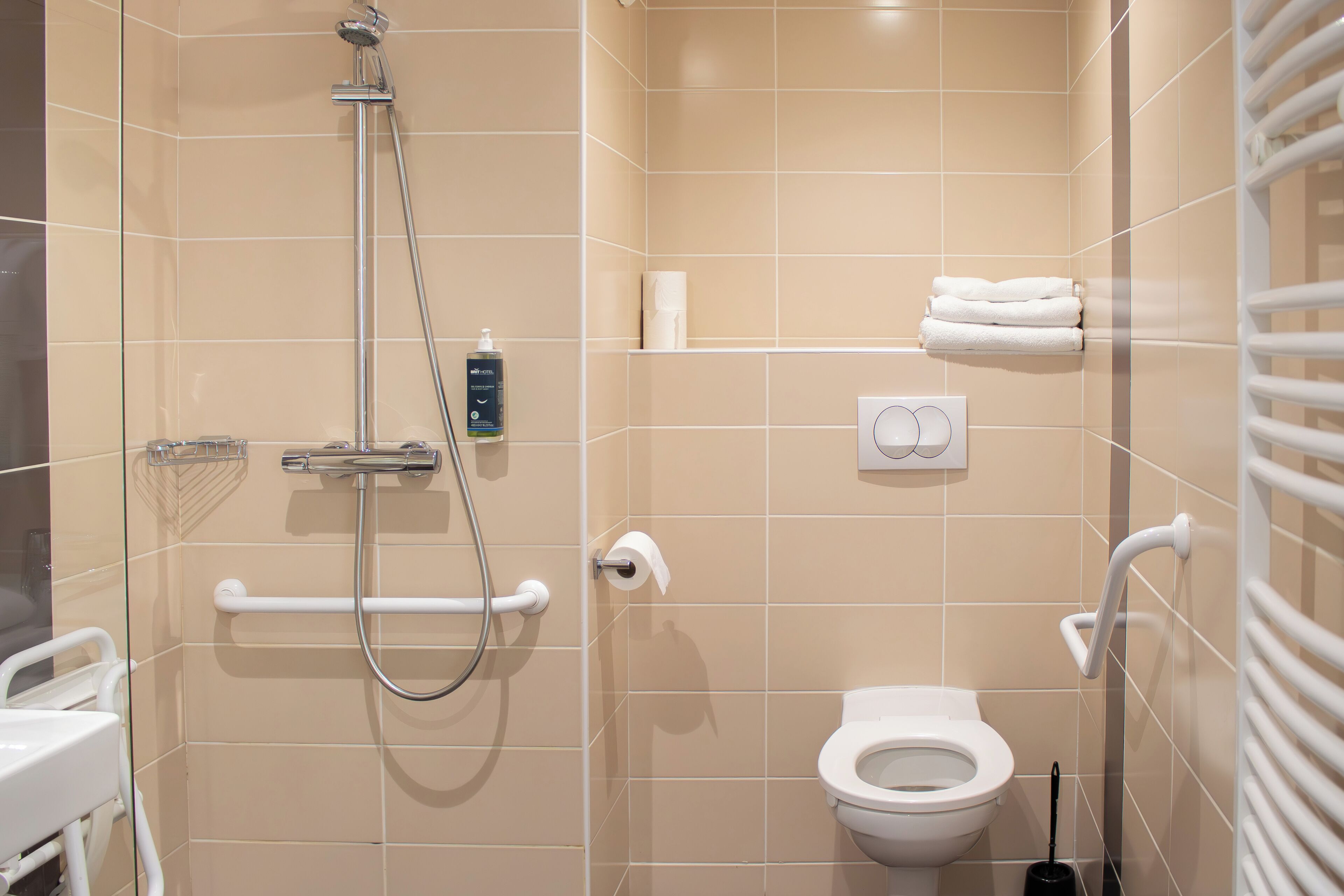 A modern bathroom with a shower, toilet, and handrails.