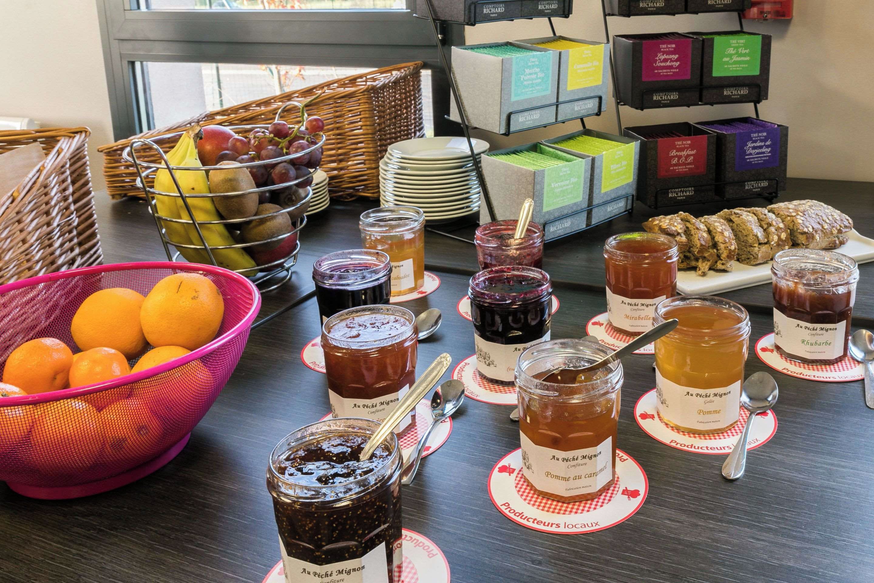 Une table de petit-déjeuner avec différentes sortes de confitures, des fruits et des viennoiseries.