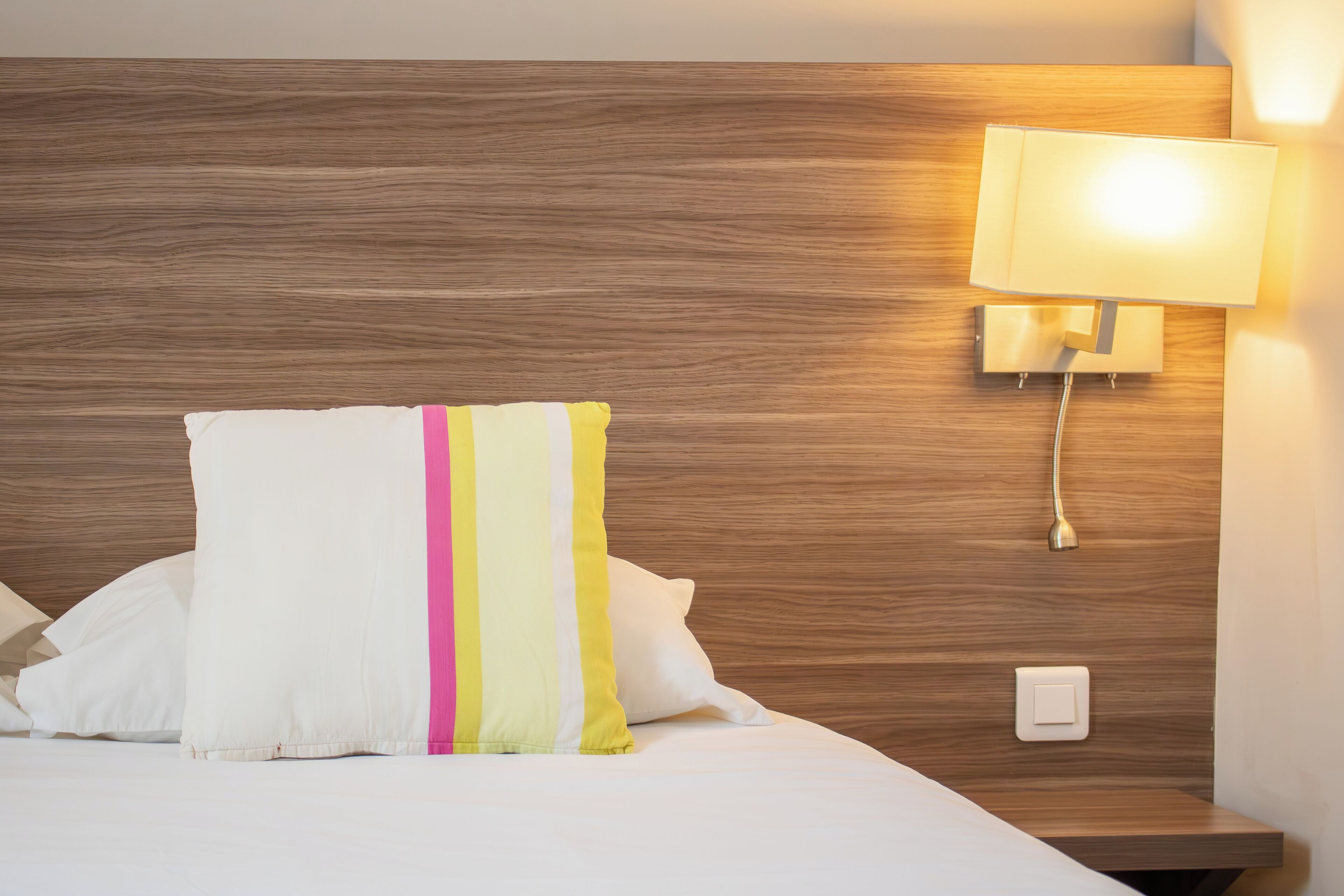 A neatly made bed with a pillow featuring a striped design, a bedside lamp, and a wooden headboard.