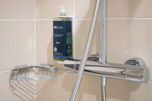 Un baño con dispensador de jabón líquido, cabezal de ducha cromado y plato de jabón de vidrio transparente.