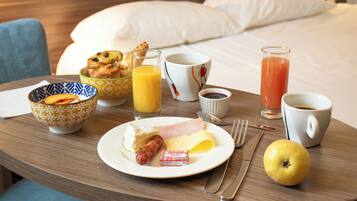 A breakfast tray with croissants, ham, cheese, a sausage, a glass of orange juice, a glass of tomato juice, a cup of coffee, a bowl of fruit, and a lemon.