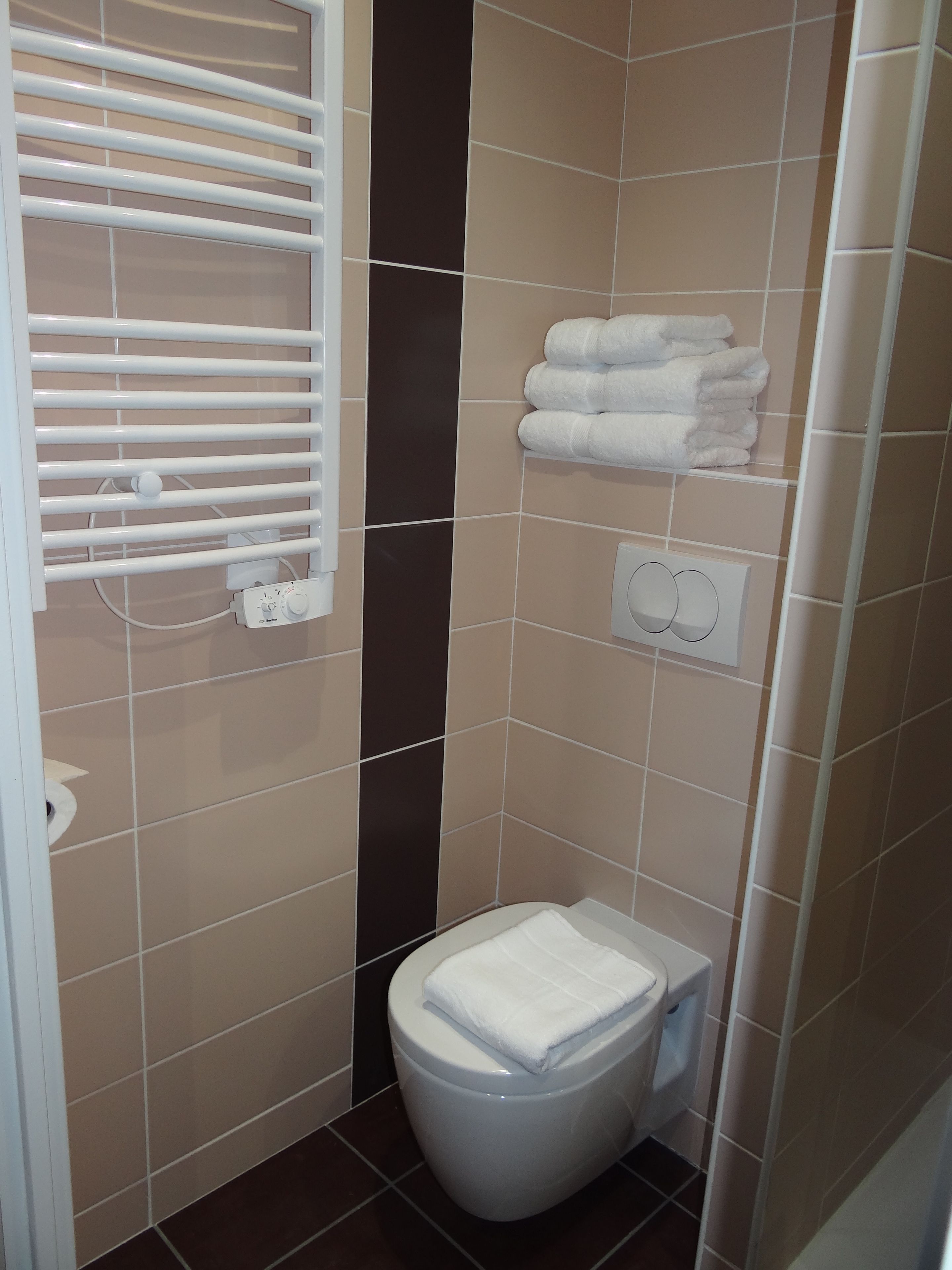 Ein kleines Badezimmer mit Toilette, Handtrockner, Papiertuchspender und einem Handtuchhalter mit gefalteten Handtüchern.