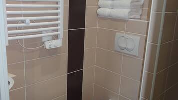 Ein kleines Badezimmer mit Toilette, Handtrockner, Papiertuchspender und einem Handtuchhalter mit gefalteten Handtüchern.