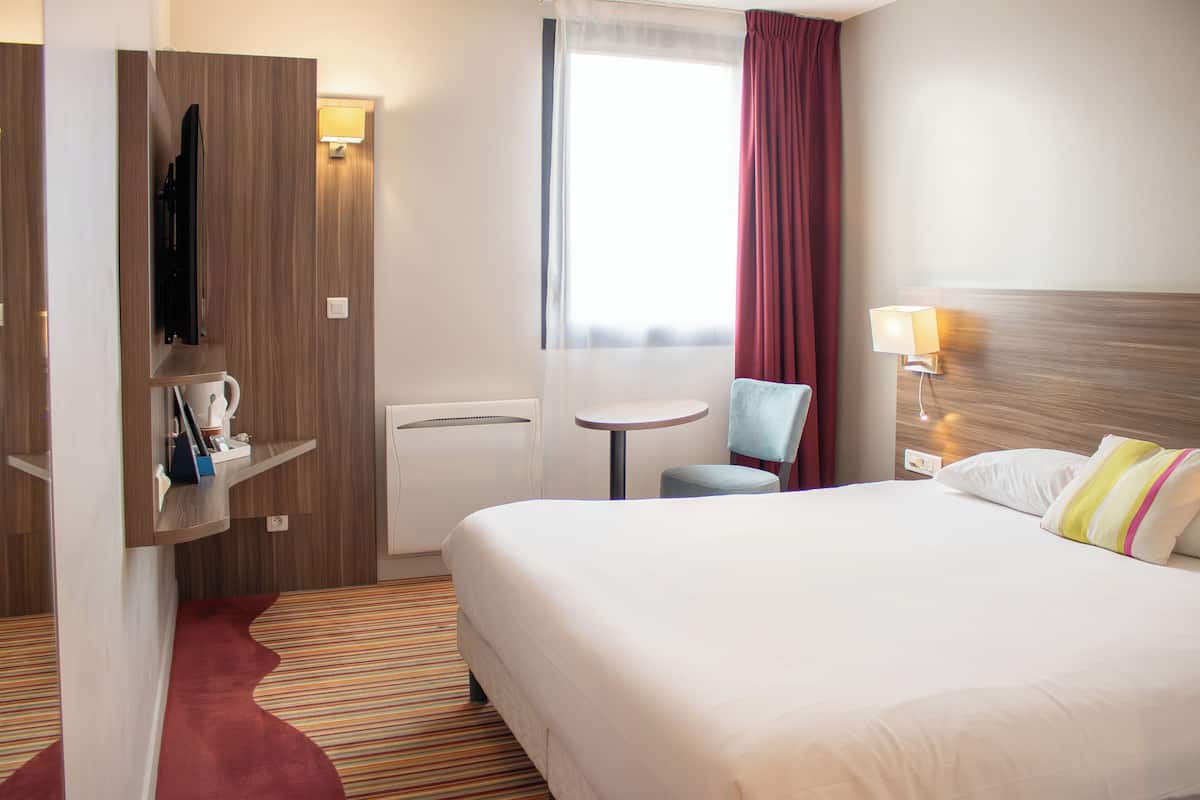 A hotel room with a large bed, a desk, a chair, a television, and a window with curtains.