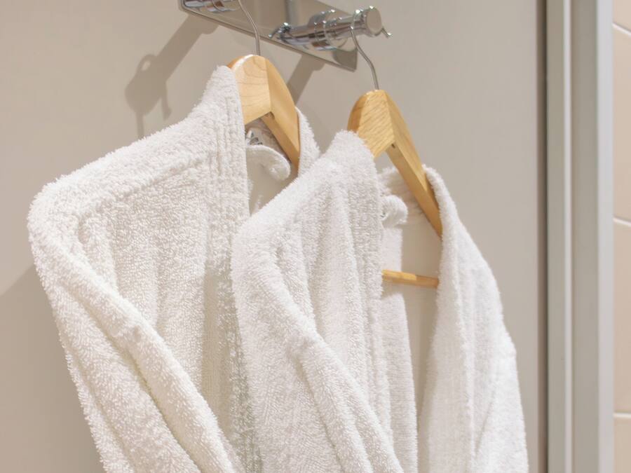 Dos batas blancas colgadas en un perchero de madera en un baño.